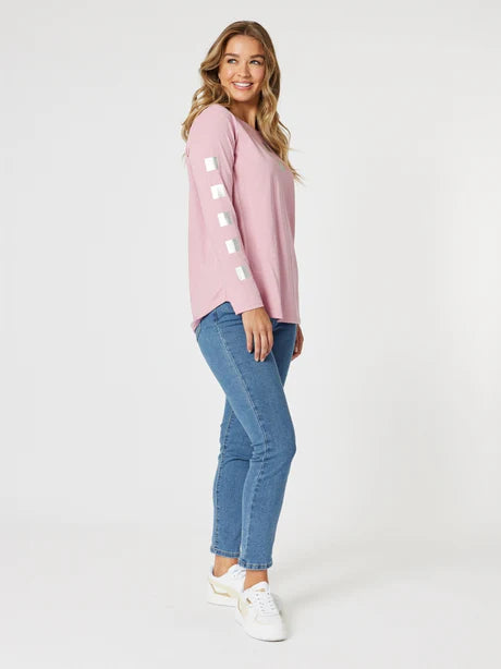 A female model wearing a pink top with heart patterns and blue slim leg jeans.