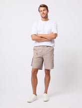 Man wearing a white shirt and beige shorts standing against a white background