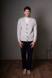 Man wearing a light gray cardigan over a white shirt, standing against a plain background.