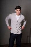Man wearing a light gray cardigan over a white shirt with dark pants against a plain background