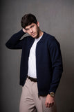 Man wearing a navy jacket over a white shirt with beige pants against a gray background