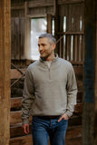 Man wearing a gray sweater and blue jeans standing in a rustic wooden setting