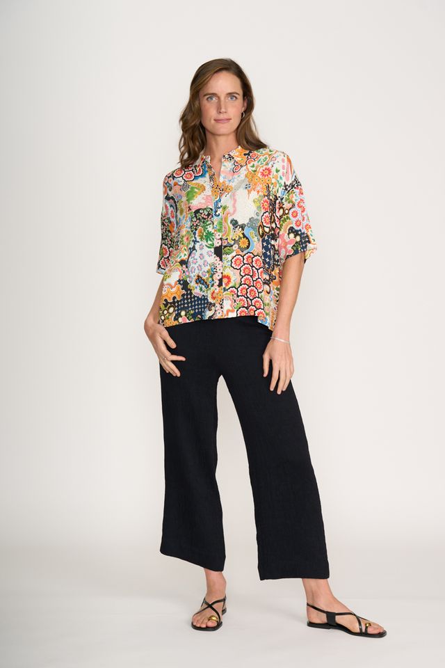 Woman wearing a colorful floral blouse and black pants on a white background