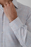 Close-up of a person adjusting the collar of a light blue checkered shirt.