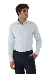 Man wearing a light blue dress shirt and dark pants against a plain background