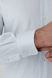 Close-up of a light blue textured shirt with rolled-up sleeve and visible buttons.