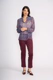 Woman wearing a patterned blouse and maroon pants on a white background