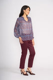 Woman wearing a patterned blouse and maroon pants on a white background