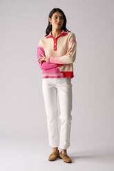Woman wearing a colorful sweater and white pants on a plain background