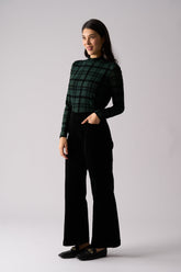 Woman wearing a green plaid shirt and black pants on a light gray background