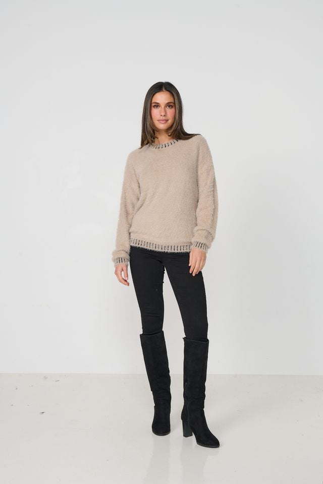 Woman wearing a beige sweater and black pants with knee-high boots on a white background