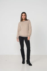 Woman wearing a beige sweater and black pants with knee-high boots on a white background