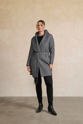 Person wearing a gray coat standing against a beige wall.