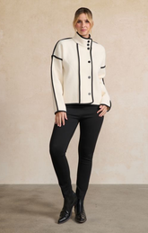 Woman wearing a white jacket with black trim and black pants against a beige background