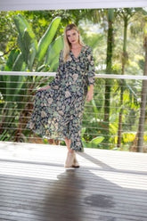 Woman in a floral dress standing on a wooden deck with greenery in the background