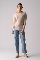 Woman wearing a beige sweater and blue jeans on a plain background