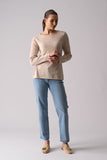 Woman wearing a beige sweater and light blue jeans on a plain background