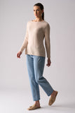 Woman wearing a beige sweater and light blue pants on a plain background