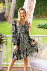 Woman in a patterned dress standing on a balcony with greenery in the background