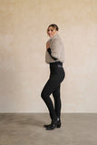 Person wearing a gray fur vest over a black outfit against a beige wall.