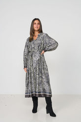A woman modeling a long-sleeved midi dress with a black and white zebra-like abstract print, paired with black knee-high boots, against a plain white studio background.