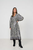A woman modeling a long-sleeved midi dress with a black and white zebra-like abstract print, paired with black knee-high boots, against a plain white studio background.