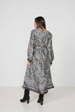 A woman viewed from the back wearing a long-sleeved, knee-length tunic dress with a black and white zebra-like abstract print and a dark gray border, paired with black ankle boots, against a plain white studio background.
