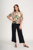 Woman wearing a colorful floral blouse and black pants on a white background