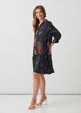 A woman modeling a short navy blue dress with a red and gold heart pattern, paired with white high-heeled sandals, set against a plain white studio background.