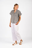 Woman wearing a gray patterned shirt and white pants on a white background