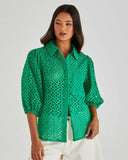 Woman wearing a green perforated blouse against a plain background