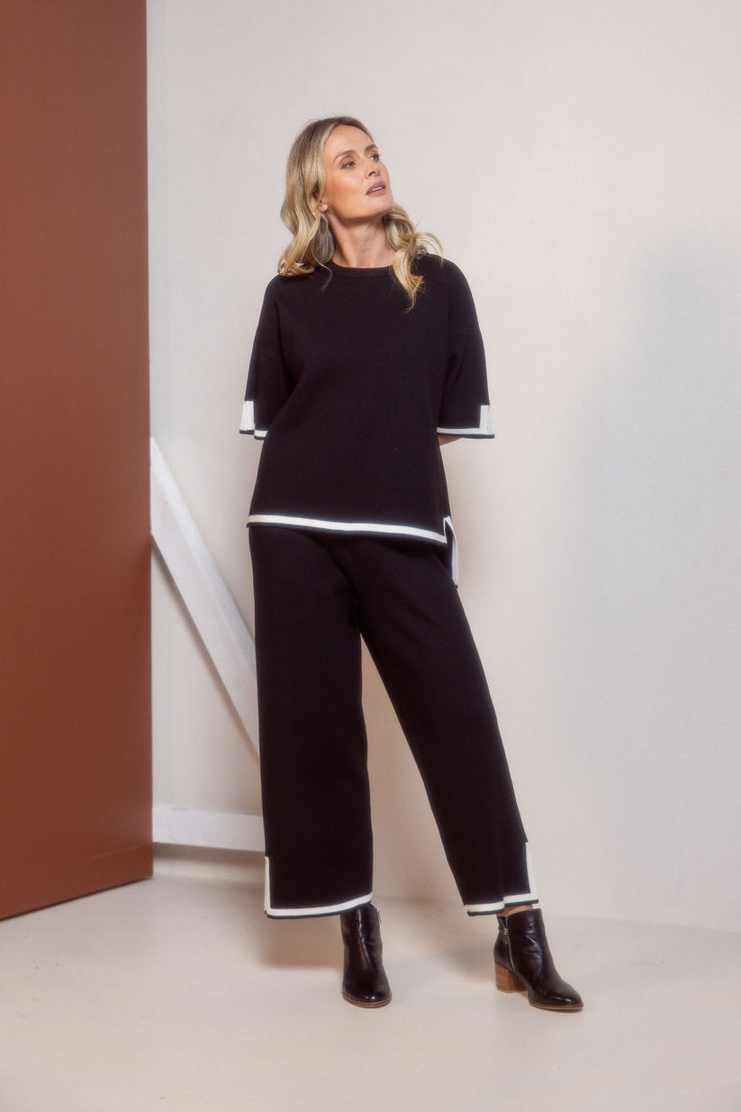 Woman wearing a black outfit with white trim standing against a plain background