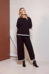 Woman wearing a black outfit with white trim standing against a plain background