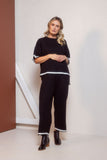 Woman wearing a black outfit with white trim standing against a neutral background