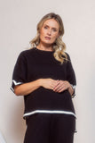 Woman wearing a black outfit with white trim standing against a neutral background