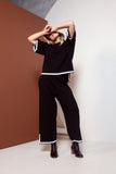 Person wearing a black outfit with white trim against a brown and white wall.