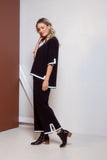 Woman wearing a black outfit with white trim standing against a white wall.