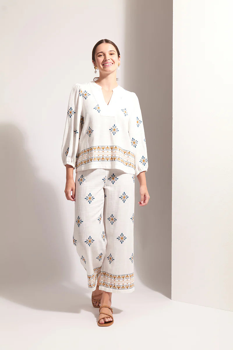 Woman wearing a white embroidered outfit against a plain background