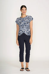 Woman wearing a patterned top and dark pants on a white background