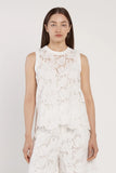 Woman wearing a white sleeveless top with floral lace details on a plain background