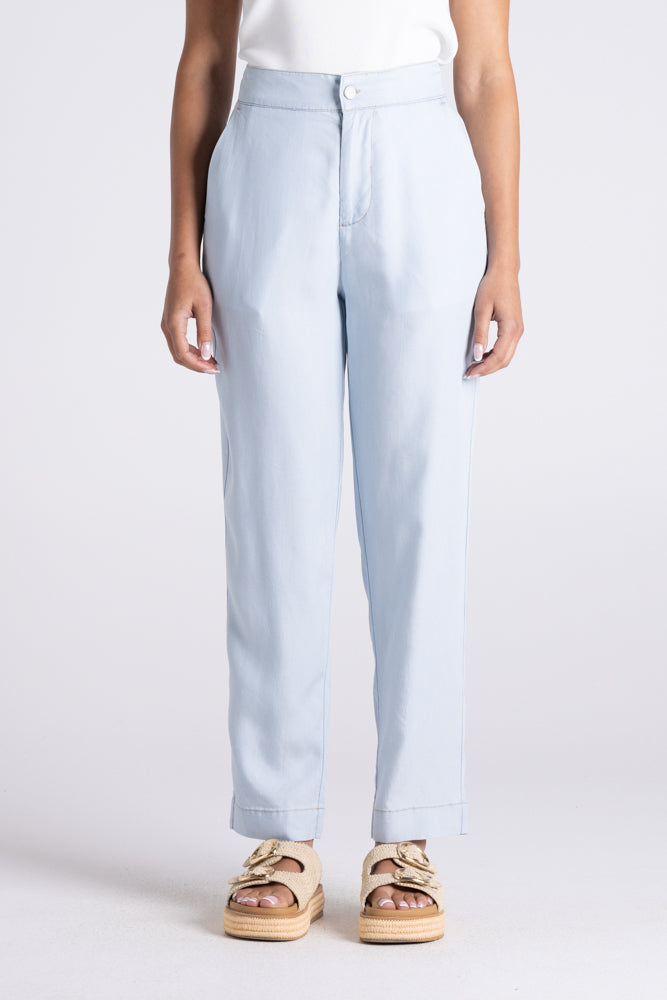 A person wearing light blue straight-leg trousers with a white top and beige double-strap sandals, shown from the waist down against a light gray studio background.