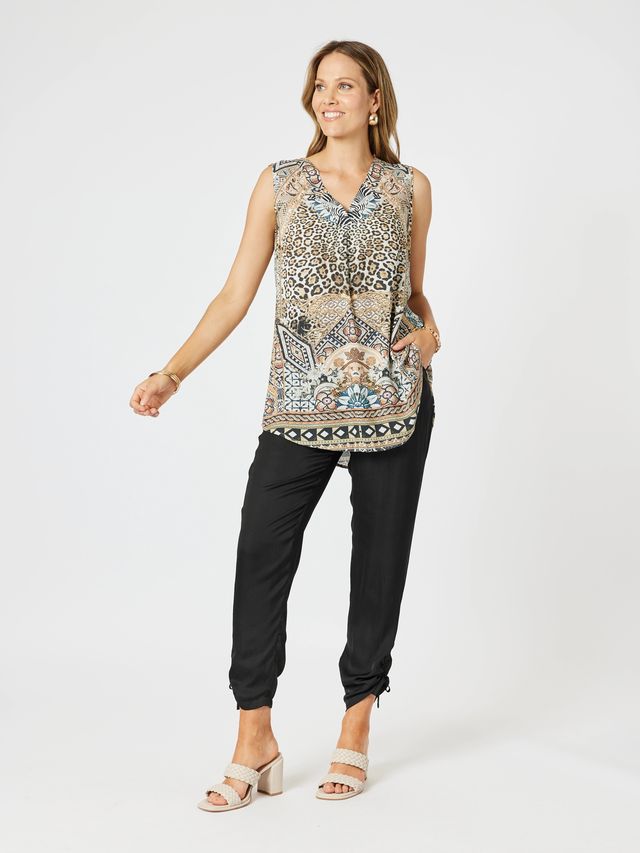 Woman wearing a patterned sleeveless top and black pants on a white background