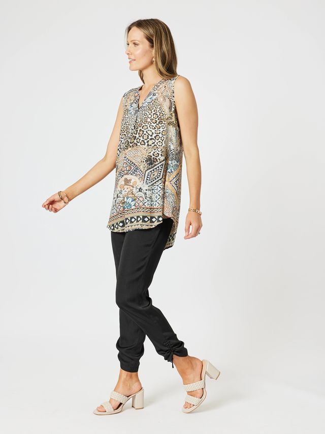 Woman wearing a sleeveless patterned top and black pants on a white background