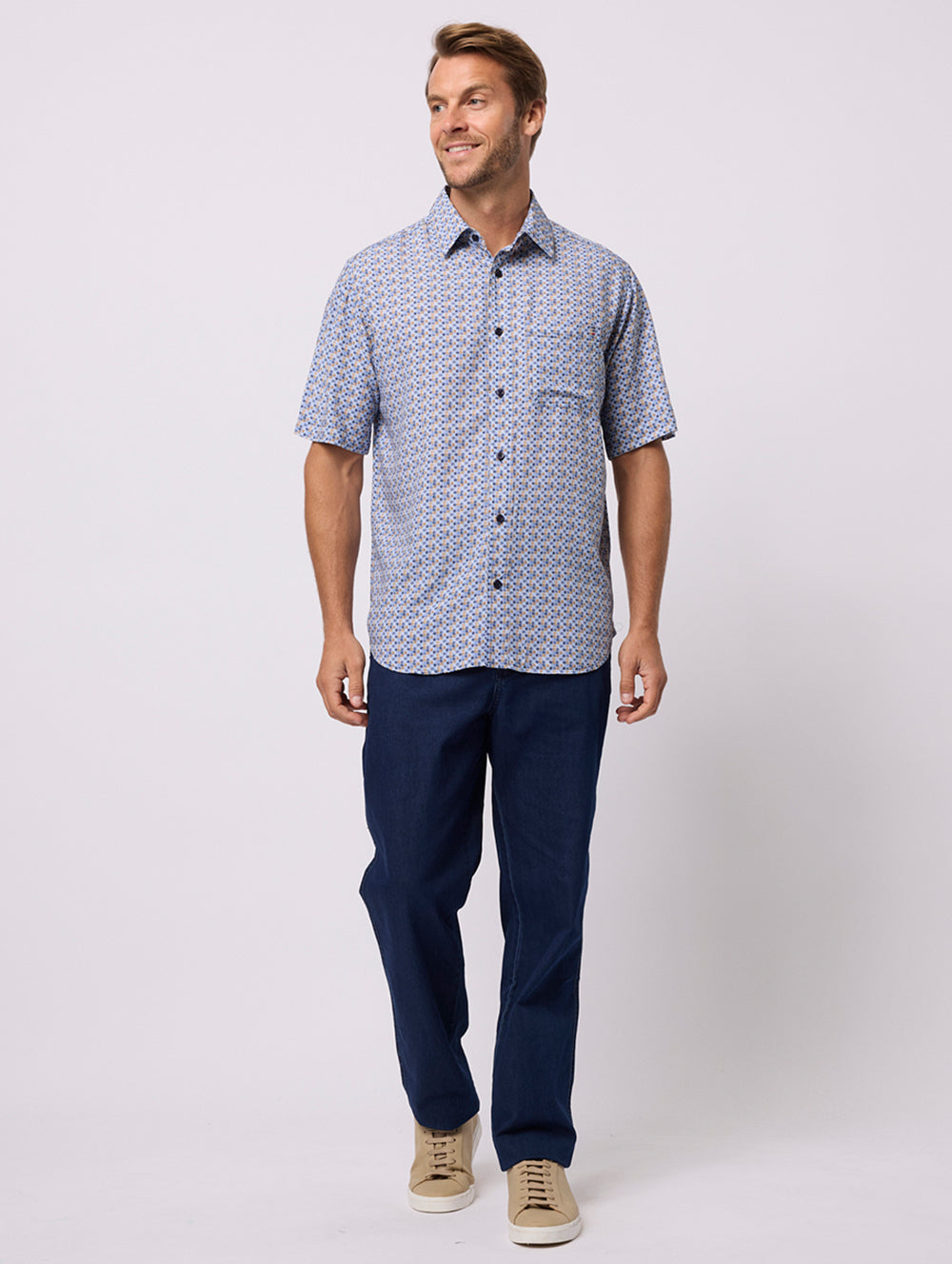 Man wearing a patterned shirt and navy pants on a white background