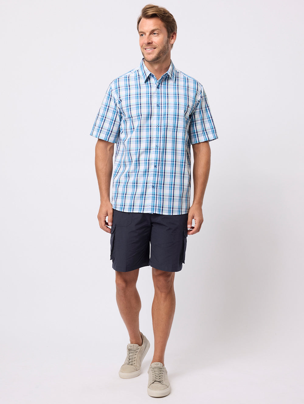 Man wearing a blue checkered shirt and black shorts on a white background