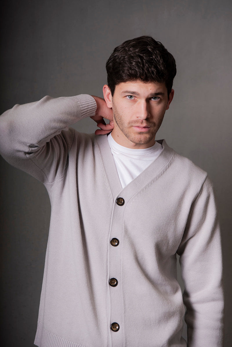 Man wearing a light gray cardigan over a white shirt against a gray background