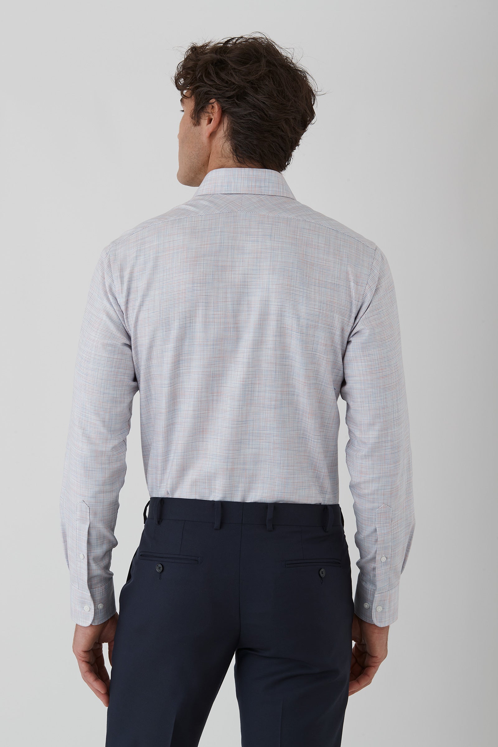 Man wearing a light gray long-sleeve shirt and dark blue pants on a white background