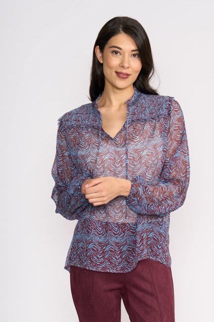 Woman wearing a patterned blouse and maroon pants on a white background