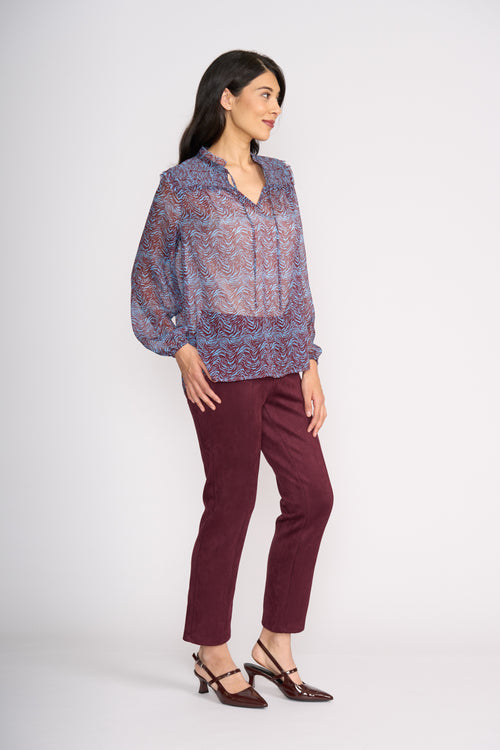Woman wearing a patterned blouse and maroon pants on a white background