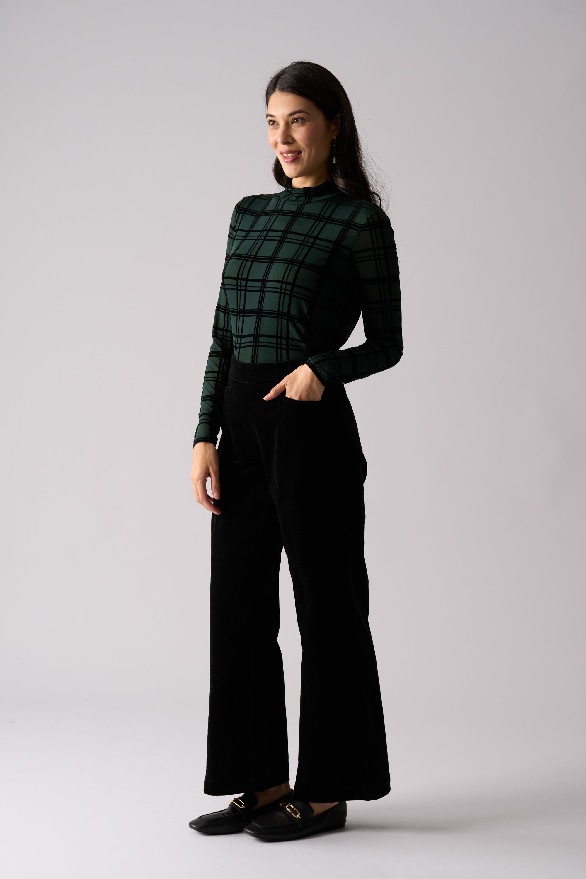 Woman wearing a green plaid shirt and black pants on a light gray background